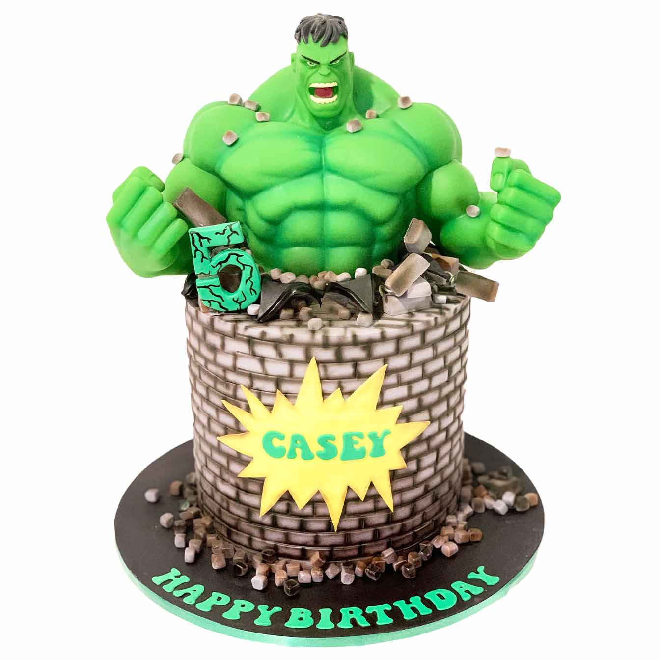 Hulk Smash Money Box Cake - A green fondant cake with a brick wall design, featuring a Hulk money box bursting out, scattered bricks, and the honouree's name in a cartoon explosion bubble, a thrilling centrepiece for superhero-themed celebrations.